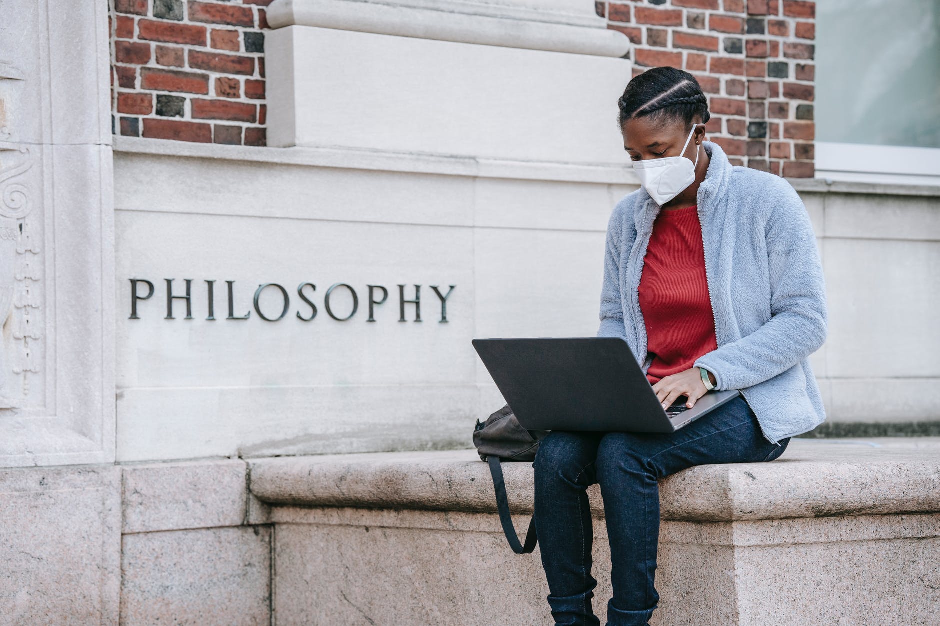 serious young black female student using laptop near university building